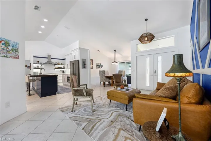 Vaulted ceilings throughout, a kitchen island with a dark finish, integrated stainless steel appliances, and tile flooring