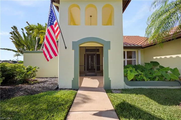 Arched entry with a screened double-door, concrete pathway, decorative architectural elements, and mature landscaping