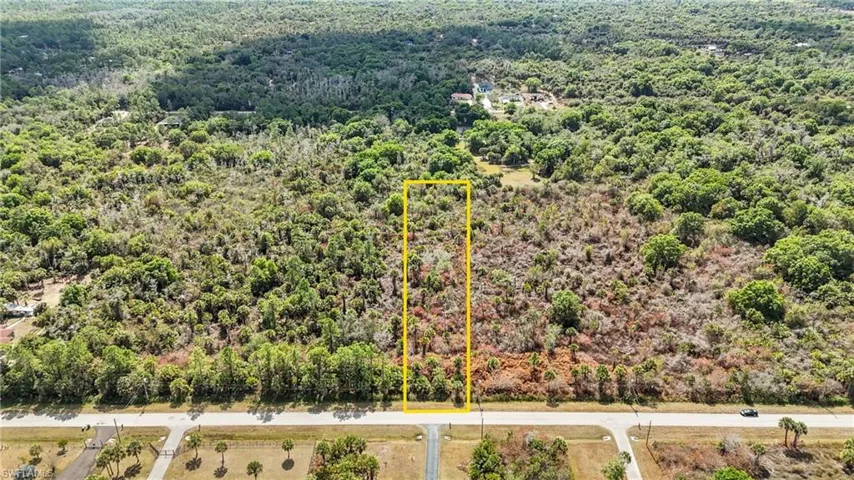 Aerial view of property and surrounding area featuring property parcel outlined and a forest