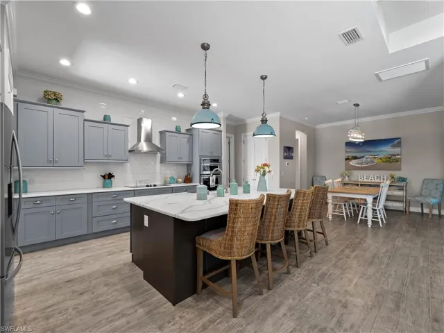 Kitchen featuring decorative backsplash, crown molding, gray cabinetry, light stone counters, and a kitchen island with sink