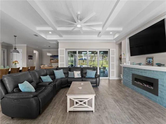 Living area featuring beamed ceiling, coffered ceiling, wood finished floors, a brick fireplace, and ceiling fan