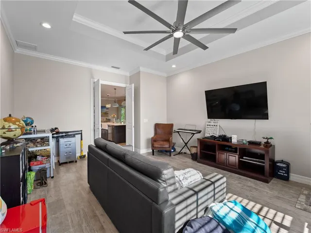 Living room with a tray ceiling, crown molding, recessed lighting, light wood finished floors, and a ceiling fan