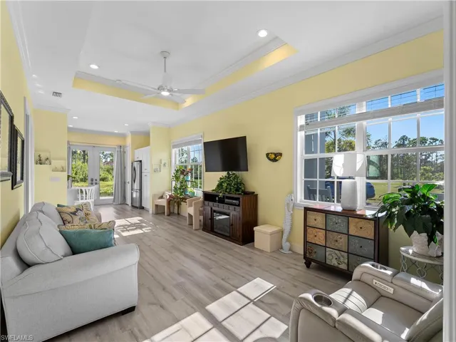 Living room with a tray ceiling, light wood-type flooring, crown molding, recessed lighting, and a ceiling fan