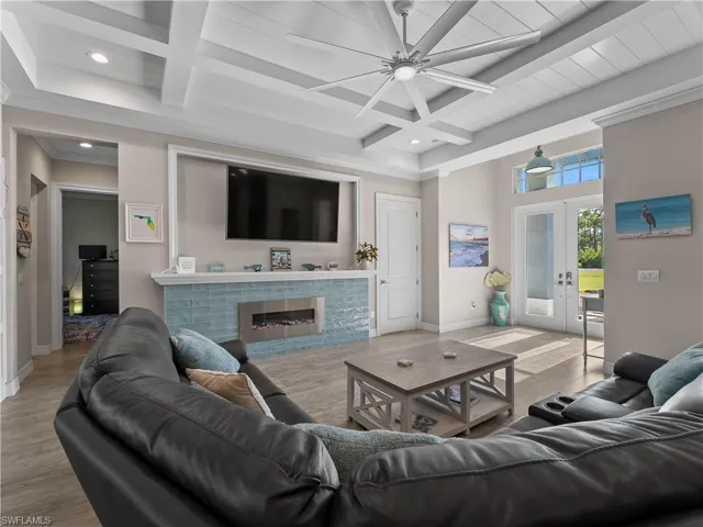 Living room featuring beam ceiling, french doors, coffered ceiling, wood finished floors, and a brick fireplace