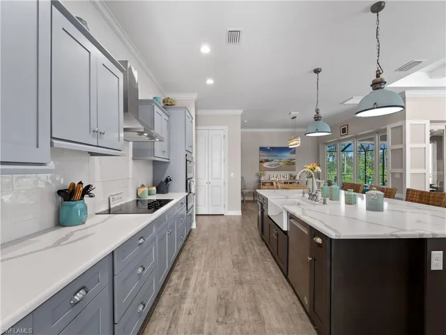Kitchen featuring decorative light fixtures, light stone countertops, ornamental molding, light wood-style flooring, and backsplash