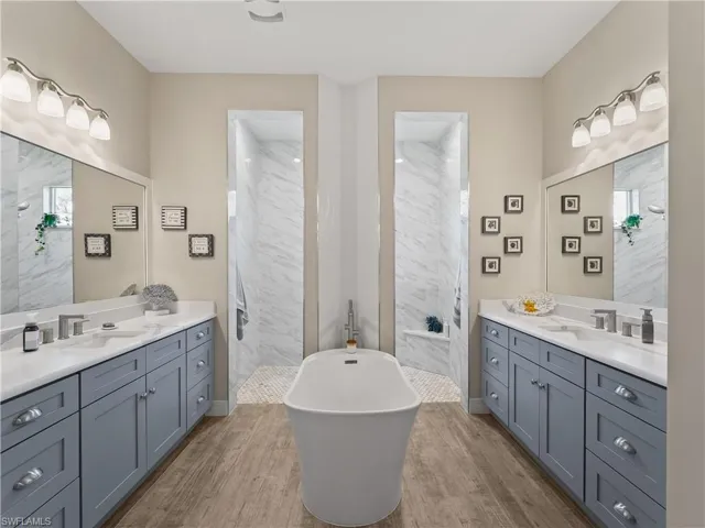 Full bath featuring light wood-style flooring, two vanities, and a walk in shower