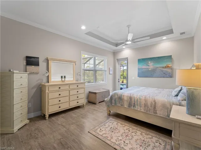 Bedroom with ornamental molding, a raised ceiling, access to outside, wood finished floors, and a ceiling fan