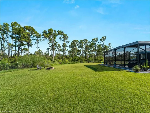 View of grassy yard with a sunroom, a lanai, and a fire pit