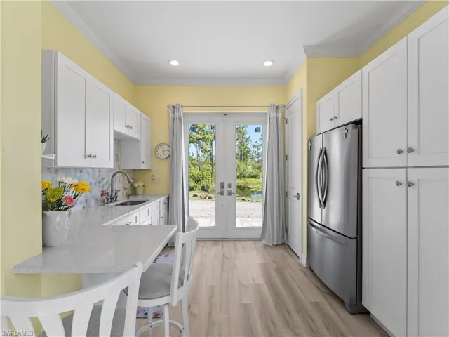 Kitchen featuring freestanding refrigerator, white cabinets, ornamental molding, light stone countertops, and a kitchen bar