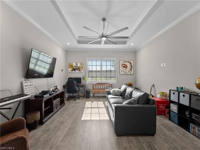 Living area with crown molding, a raised ceiling, light wood-style flooring, recessed lighting, and a ceiling fan