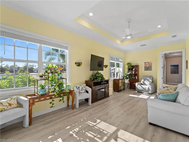 Living area with a raised ceiling, crown molding, light wood-style floors, recessed lighting, and ceiling fan