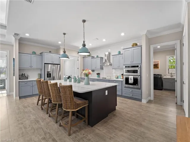 Kitchen with healthy amount of natural light, a kitchen bar, a kitchen island with sink, hanging light fixtures, and crown molding