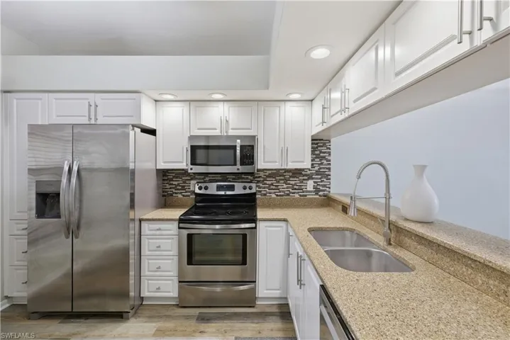 Kitchen with stainless steel appliances, white cabinets, tasteful backsplash, granite counters