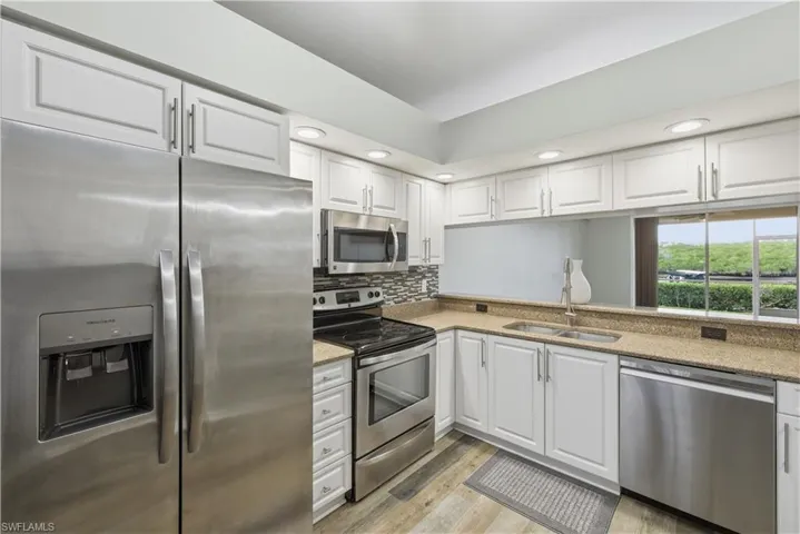 Kitchen with stainless steel appliances, white cabinets, granite counters, light wood-style flooring