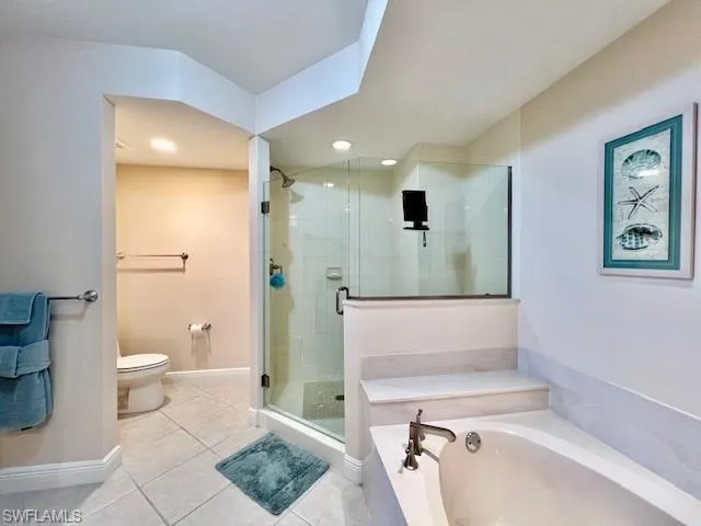 Full bath featuring tile patterned flooring, baseboards, toilet, a garden tub, and a stall shower