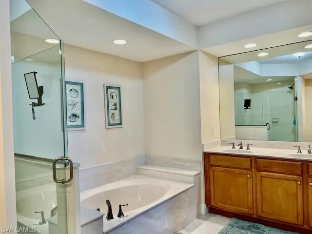 Bathroom featuring double vanity, a shower stall, a garden tub, and a sink