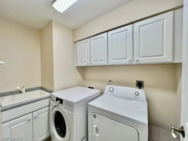Clothes washing area with separate washer and dryer, cabinet space, and a sink
