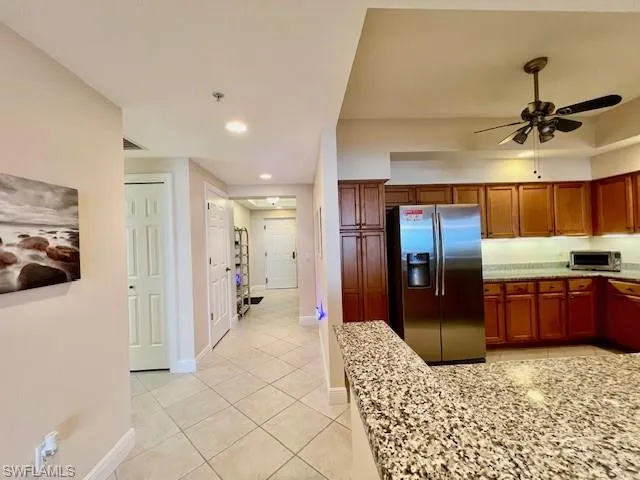 Kitchen with brown cabinetry, stainless steel fridge with ice dispenser, light tile patterned floors, baseboards, and ceiling fan