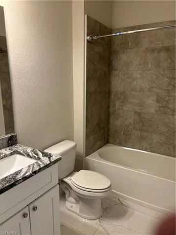 Full bathroom featuring tile flooring, tiled shower / bath, vanity, and toilet