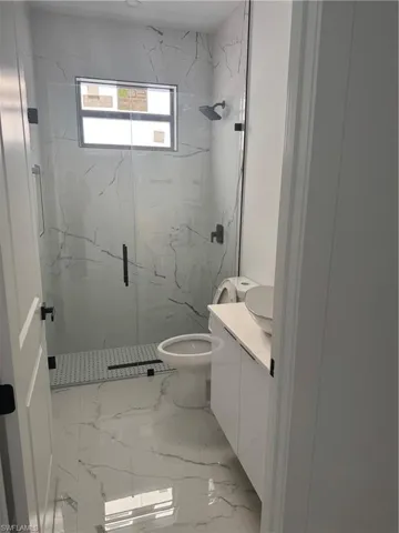 Bathroom with toilet, marble finish floor, vanity, and a marble finish shower