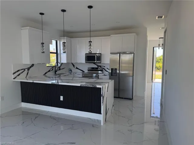 Kitchen featuring a peninsula, visible vents, appliances with stainless steel finishes, decorative light fixtures, and baseboards
