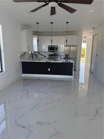 Kitchen with range, ceiling fan, refrigerator, white cabinets, and baseboards