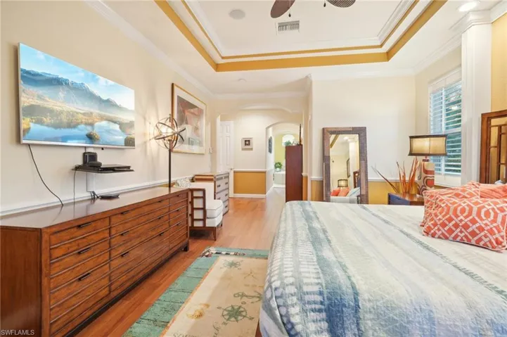 Bedroom with light wood-style flooring, arched walkways, a tray ceiling, and visible vents
