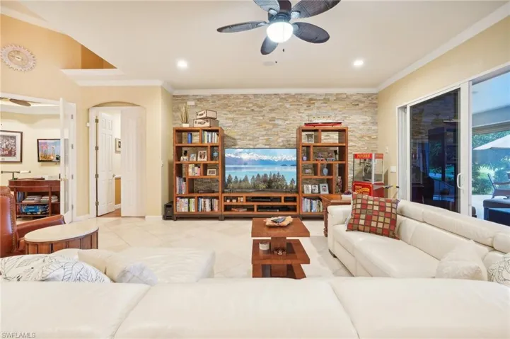 Living area featuring arched walkways, light tile patterned floors, ceiling fan, and crown molding