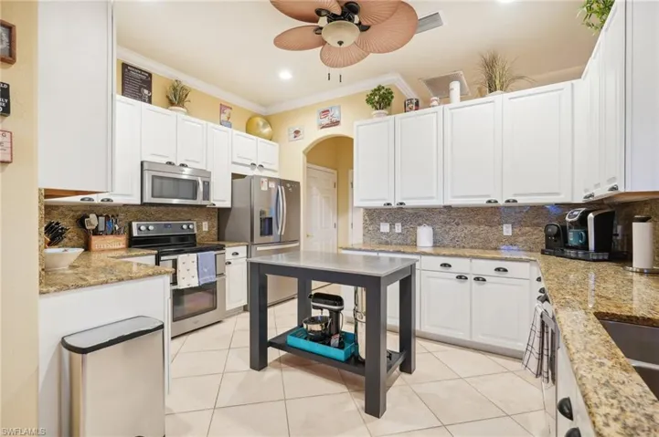 Kitchen featuring decorative backsplash, appliances with stainless steel finishes, crown molding, and ceiling fan