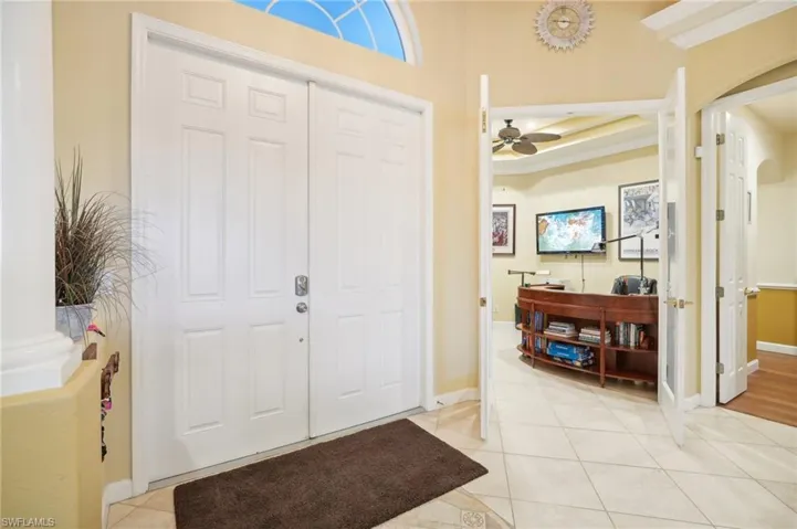 Entryway with light tile patterned flooring, crown molding, baseboards, a ceiling fan, and arched walkways
