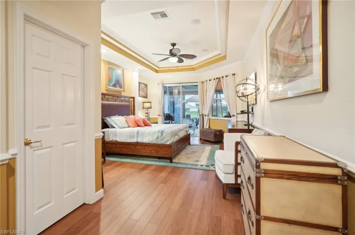 Bedroom featuring a tray ceiling, access to exterior, visible vents, light wood-style floors, and ornamental molding