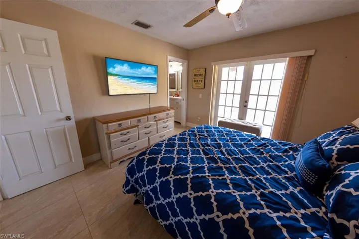 Bedroom featuring french doors, ensuite bath, ceiling fan, and a textured ceiling