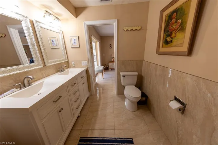 Bathroom with double vanity, tile walls, and a wainscoted wall