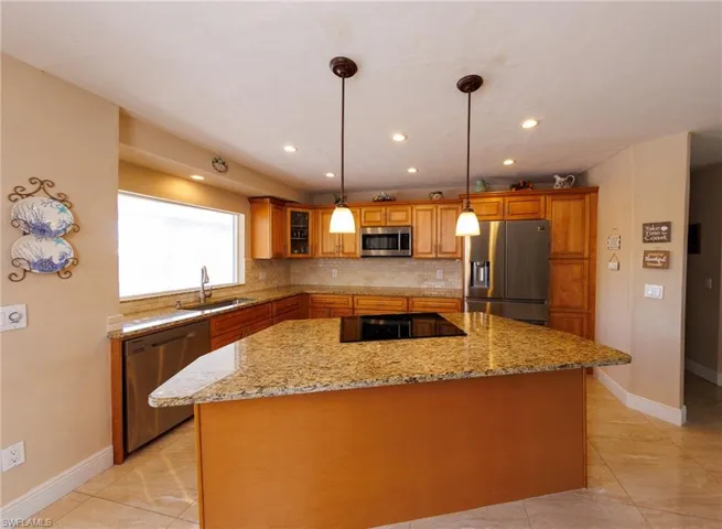 Kitchen with stainless steel appliances, a center island, decorative light fixtures, light stone counters, and decorative backsplash