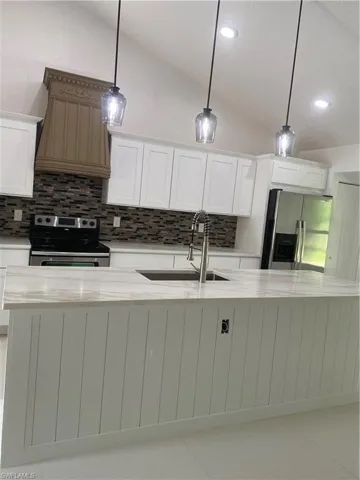 Kitchen featuring stove, fridge, vaulted ceiling, decorative backsplash, and a sink
