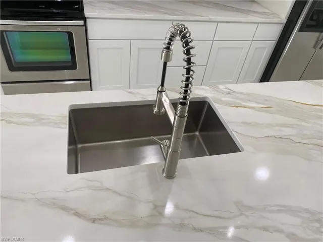 Kitchen featuring stainless steel appliances, vaulted ceiling, a sink, backsplash, and white cabinetry