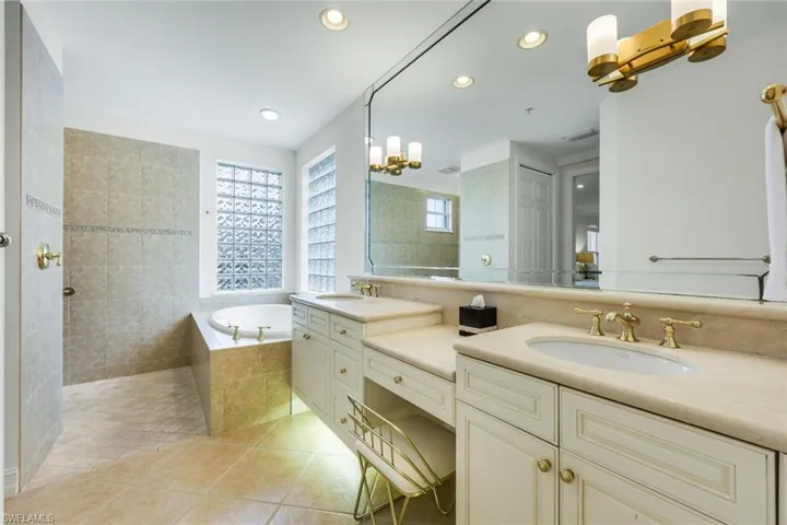 Bathroom featuring a garden tub, light tile patterned flooring, double vanity, suspended lighting, and a walk in shower