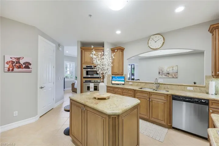 Kitchen featuring stainless steel appliances, backsplash, light tile patterned floors, a center island, and light stone counters