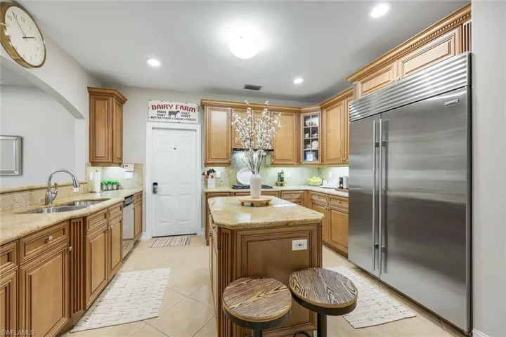 Kitchen with stainless steel appliances, a center island, light stone counters, decorative backsplash, and glass insert cabinets
