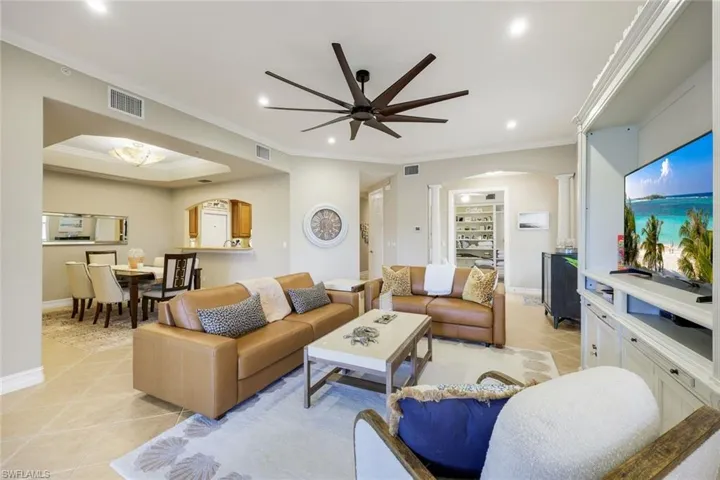 Living room featuring light tile patterned floors, arched walkways, crown molding, a ceiling fan, and built in shelves