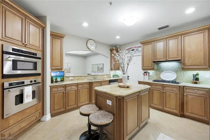 Kitchen with stainless steel appliances, light tile patterned flooring, wood finish cabinets, light stone countertops, and recessed lighting