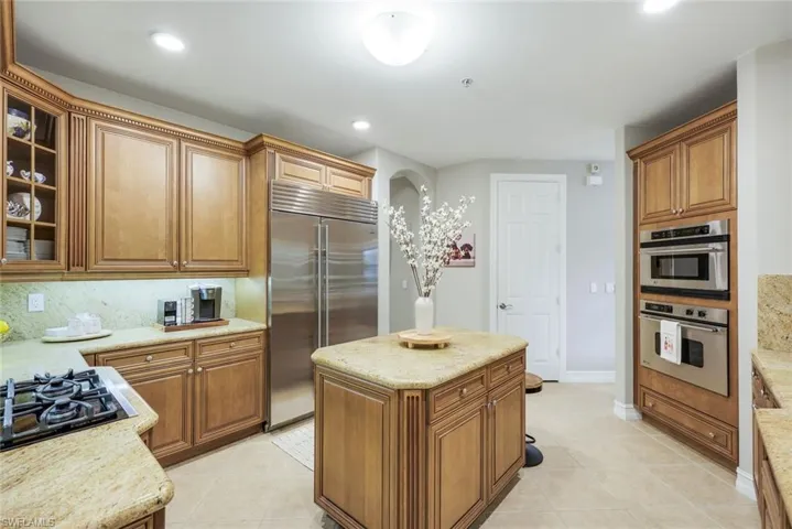 Kitchen featuring stainless steel appliances, light tile patterned flooring, glass fronted cabinets, wood finish cabinets, and a center island