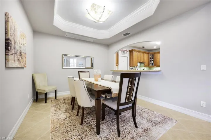 Dining space with a raised ceiling, ornamental molding, light tile patterned flooring, and arched walkways
