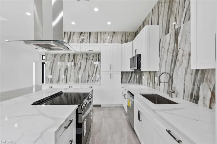 Kitchen featuring appliances with stainless steel finishes, white cabinets, light stone counters, and island range hood