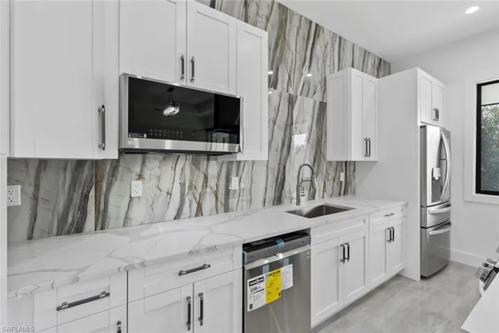 Kitchen with stainless steel appliances, backsplash, sink, light stone countertops, and white cabinets