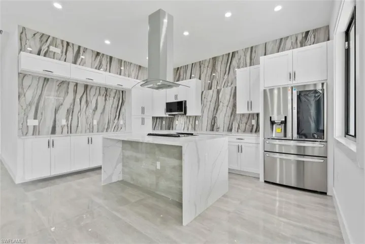 Kitchen with island exhaust hood, white cabinets, light stone counters, a kitchen island, and stainless steel appliances