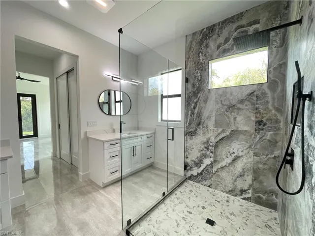 Bathroom featuring tile walls, vanity, ceiling fan, and a shower with shower door