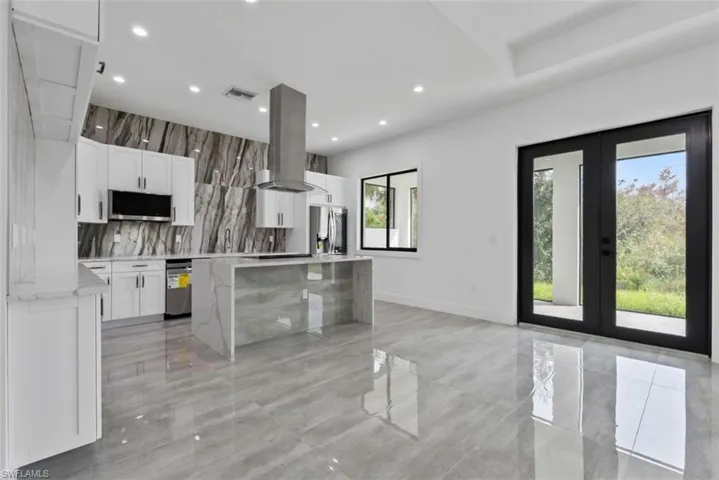 Kitchen with french doors, stainless steel appliances, range hood, a center island, and white cabinets