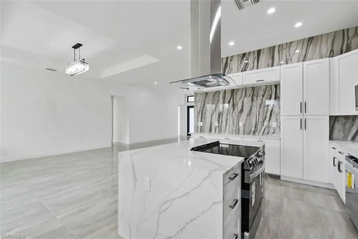 Kitchen with decorative backsplash, hanging light fixtures, appliances with stainless steel finishes, white cabinetry, and light stone counters