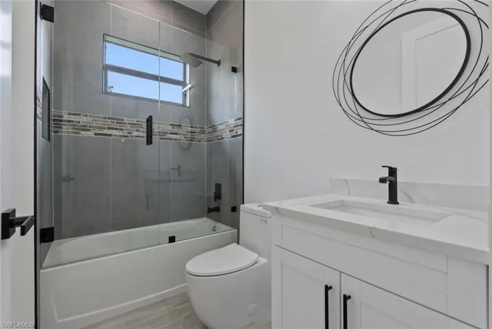 Full bathroom with vanity, toilet, hardwood / wood-style flooring, and combined bath / shower with glass door